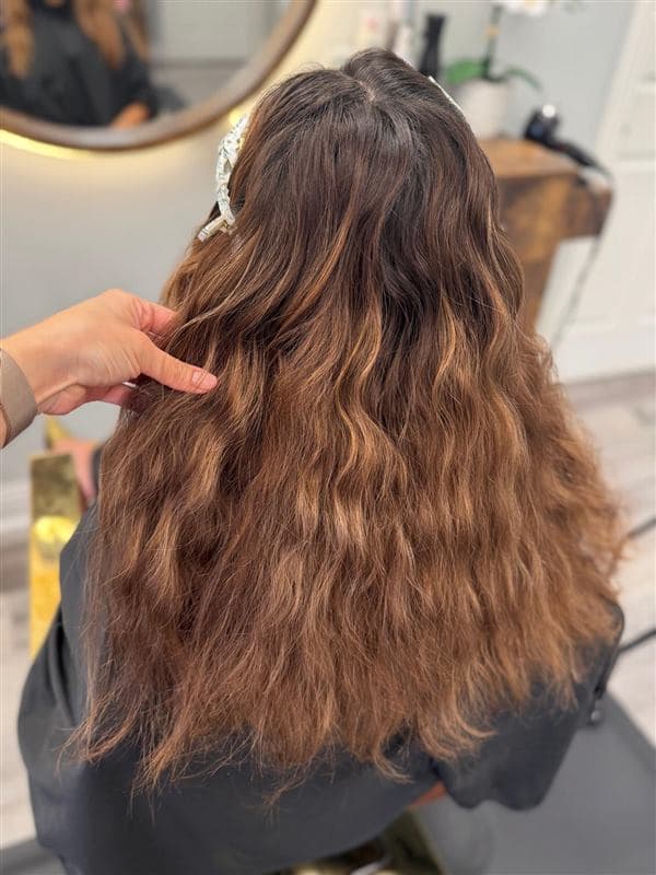 Melena larga con ondas cobrizas y balayage caramelo, vista desde atrás en el salón