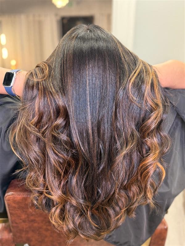 Rizos definidos con tonos caramelo y chocolate sobre base oscura