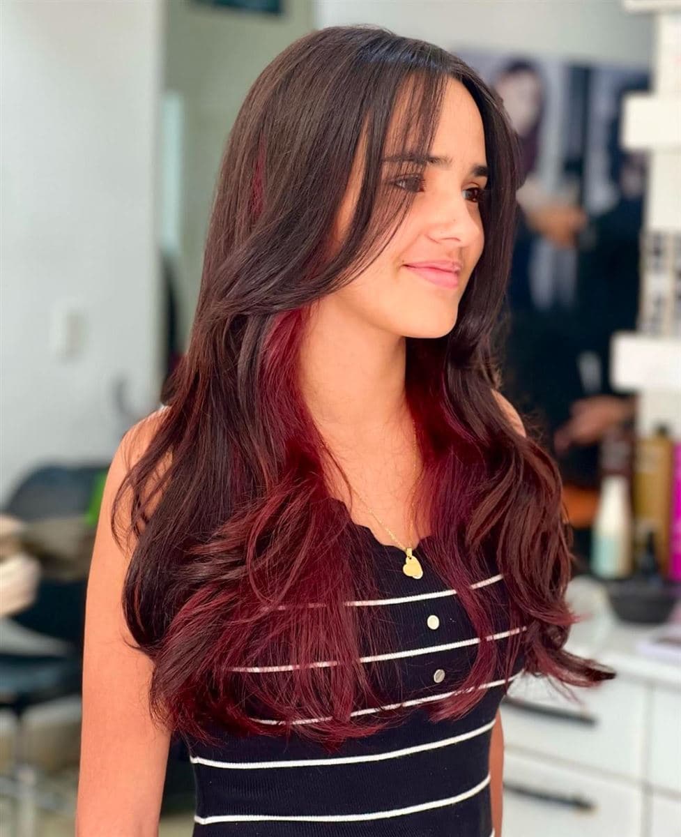 Melena oscura con mechas rojas interiores estilo peekaboo